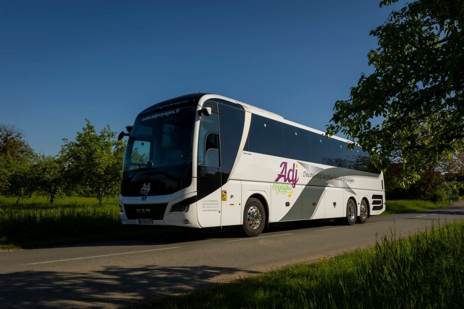Autocar MAN d’ADJ Voyages sur une route de campagne sous un ciel bleu